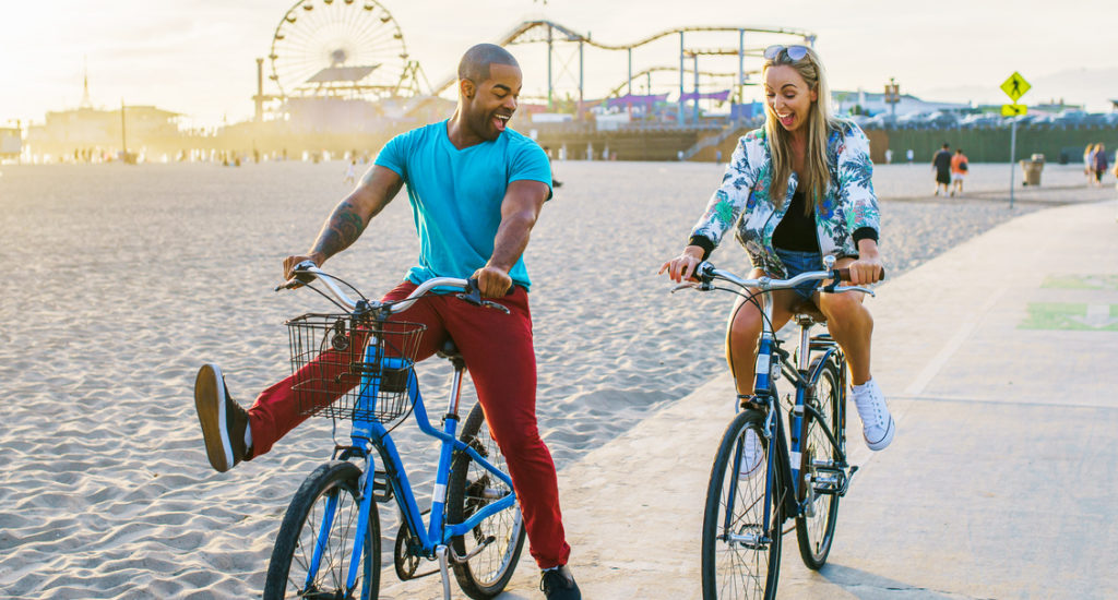 couple having fun riding bikes together at santa monica california near sunset